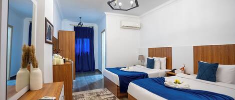 A hotel room with two beds, a wooden desk, a mirror, and a chandelier.