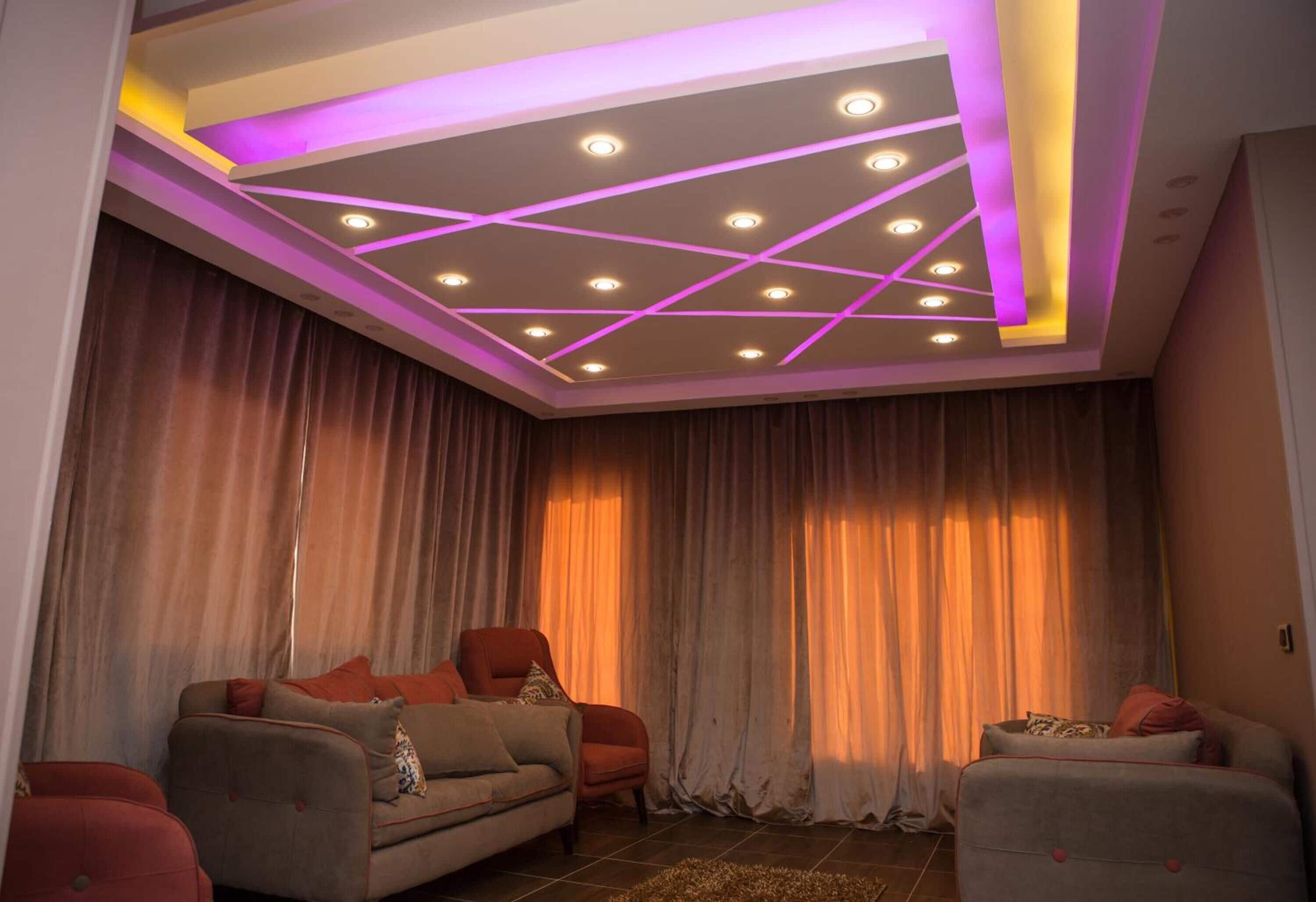 A living room with a modern ceiling design, a sofa set, and curtains.