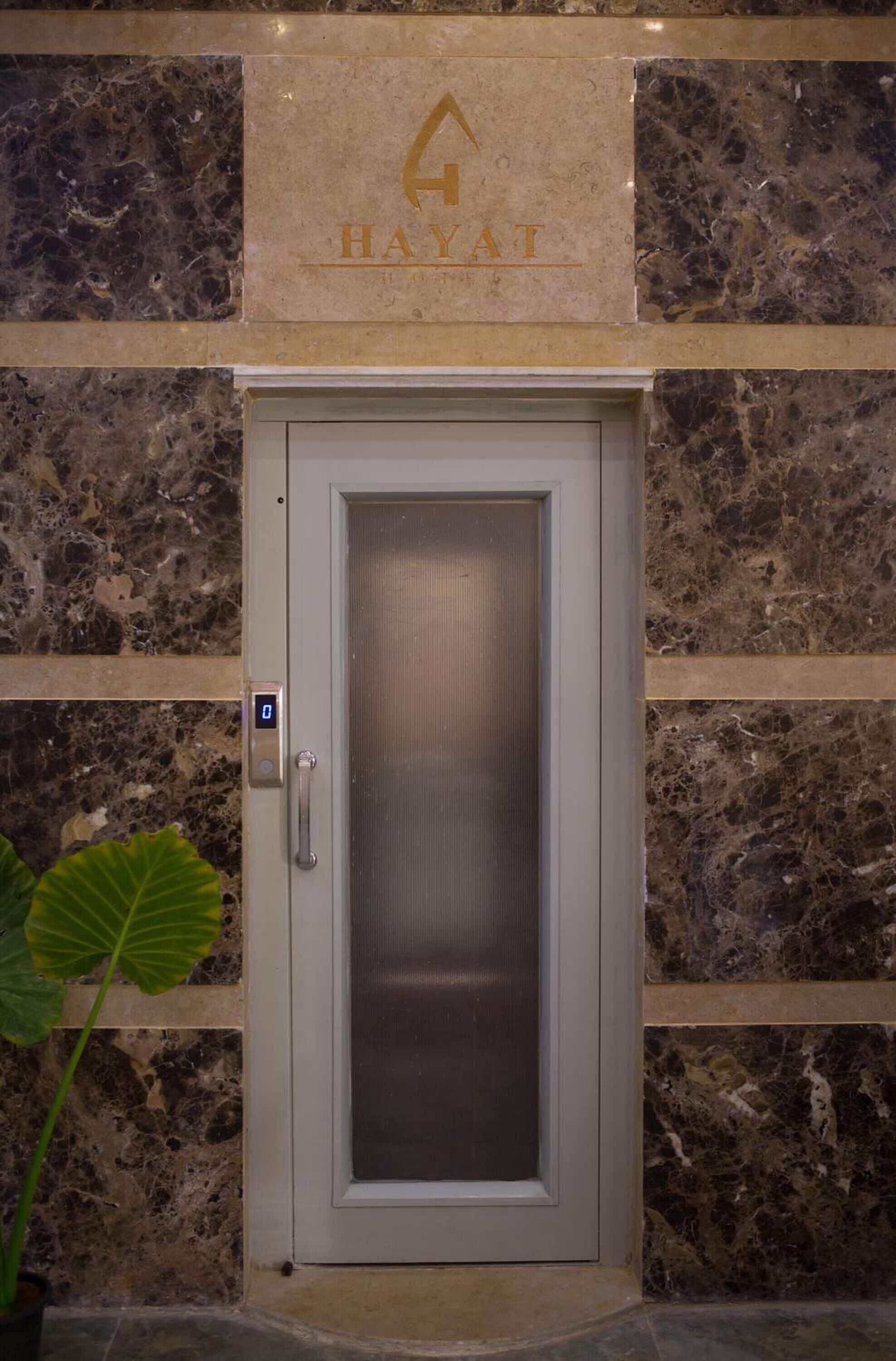 A modern elevator with a digital display, a metallic door, and a marble wall with a 'HAYAT' sign above it.