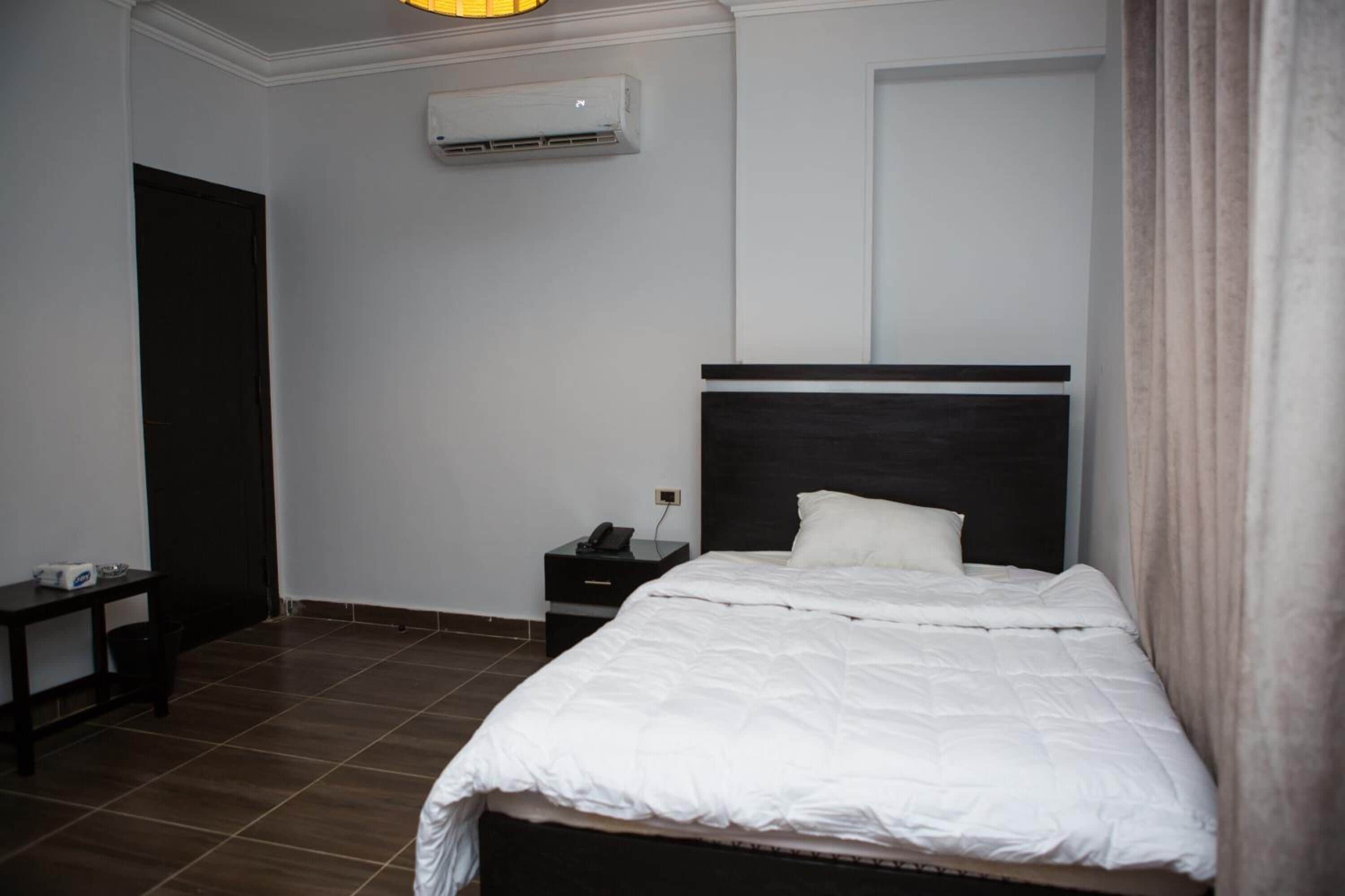 A hotel room with a bed, a nightstand, a desk, and an air conditioning unit.