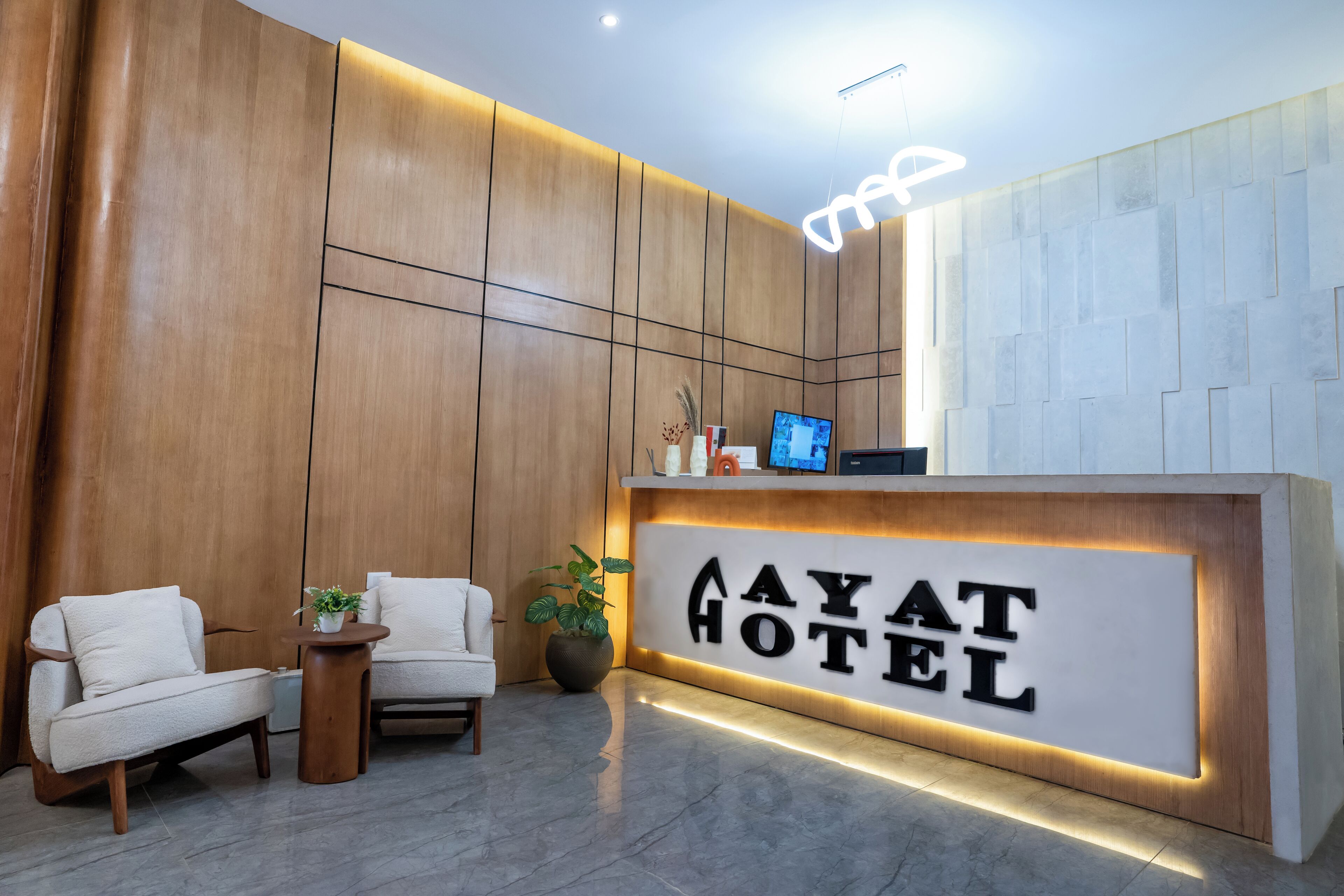 A reception area with a wooden wall, a reception desk, two white armchairs, a small table, and a potted plant.