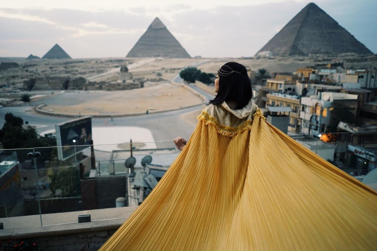 Une vue des pyramides, prise depuis un point de vue élevé, surplombant un paysage désertique avec une étendue d’eau et des bâtiments au premier plan.
