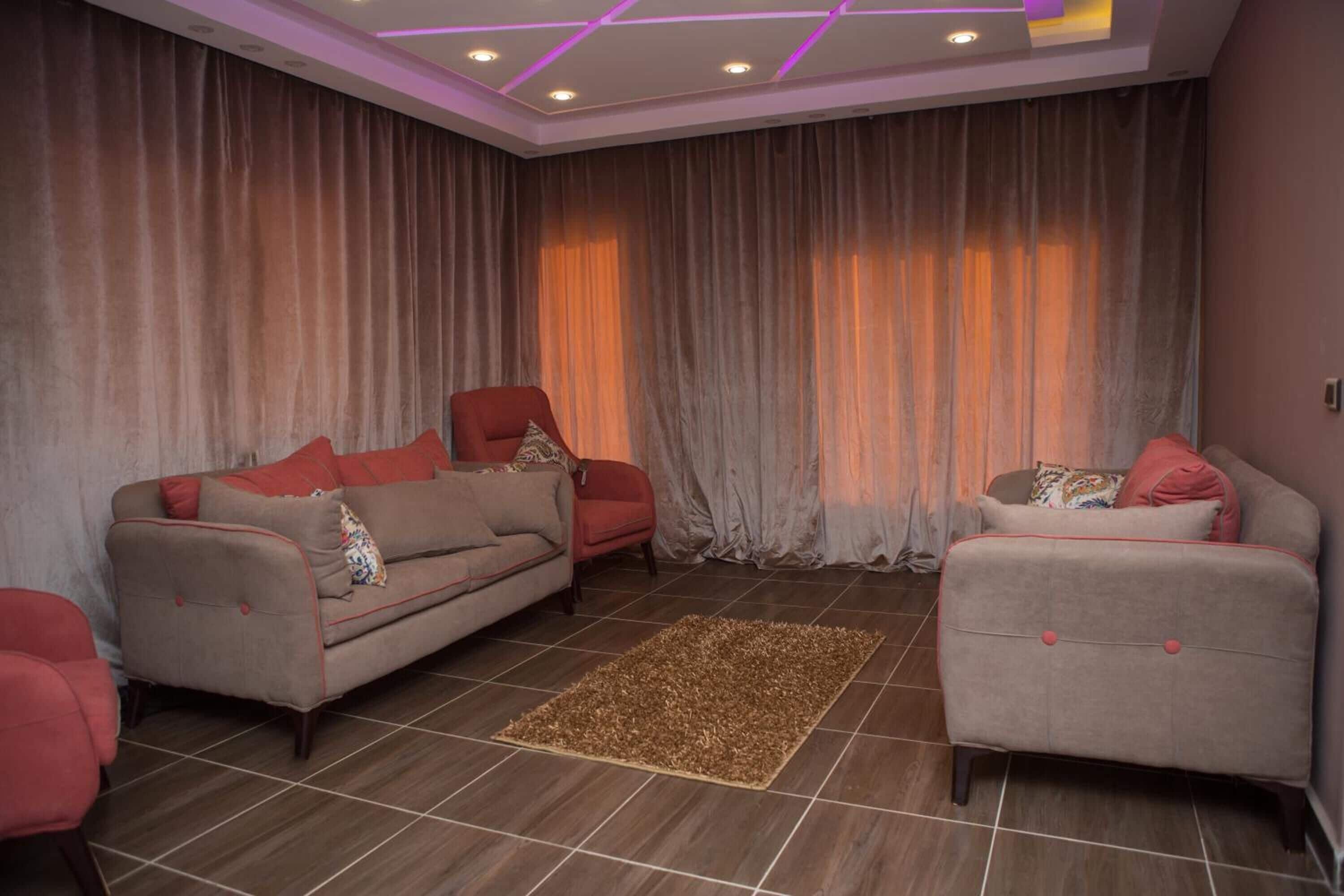 Uma sala de estar com dois sofás, uma poltrona vermelha e um tapete estampado.