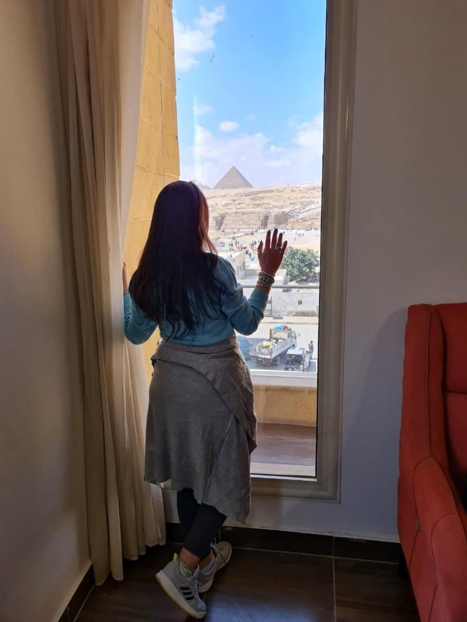 A person standing by a window with a view of a pyramid.