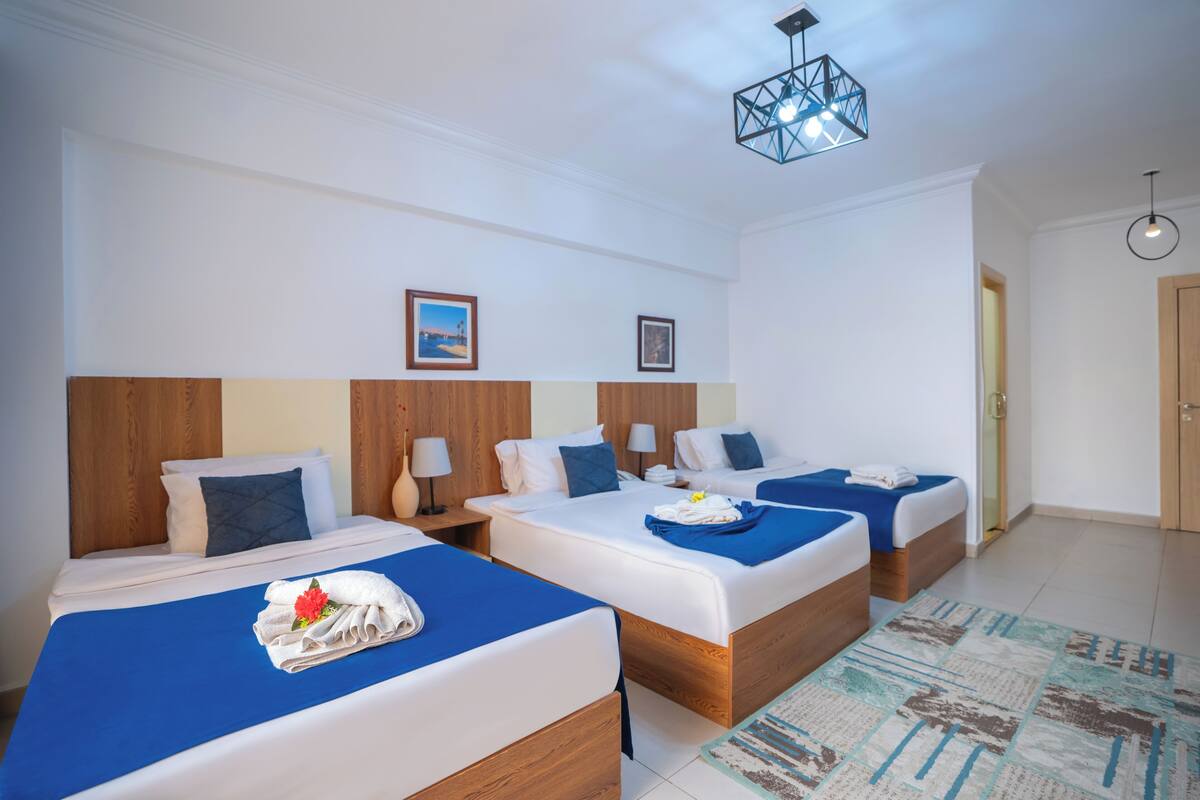 A hotel room with three beds, wooden headboards, and a patterned rug.