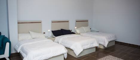 A hotel room with three beds, a small seating area, and a ceiling light fixture.