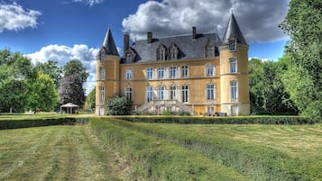 A large, historic building with multiple towers and a well-maintained garden.