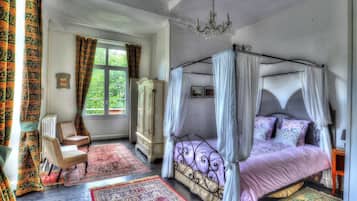 Een slaapkamer met een hemelbed, een zithoek met een stoel en een tafel, en een groot raam met gordijnen.