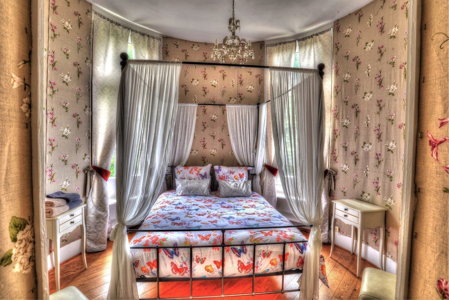 Una cama con dosel y cortinas, ropa de cama floral, una mesita de noche.