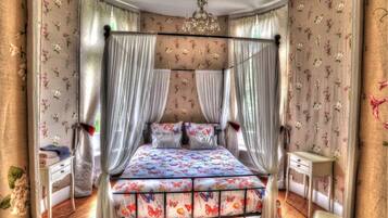 Una cama con dosel y cortinas, ropa de cama floral, una mesita de noche.
