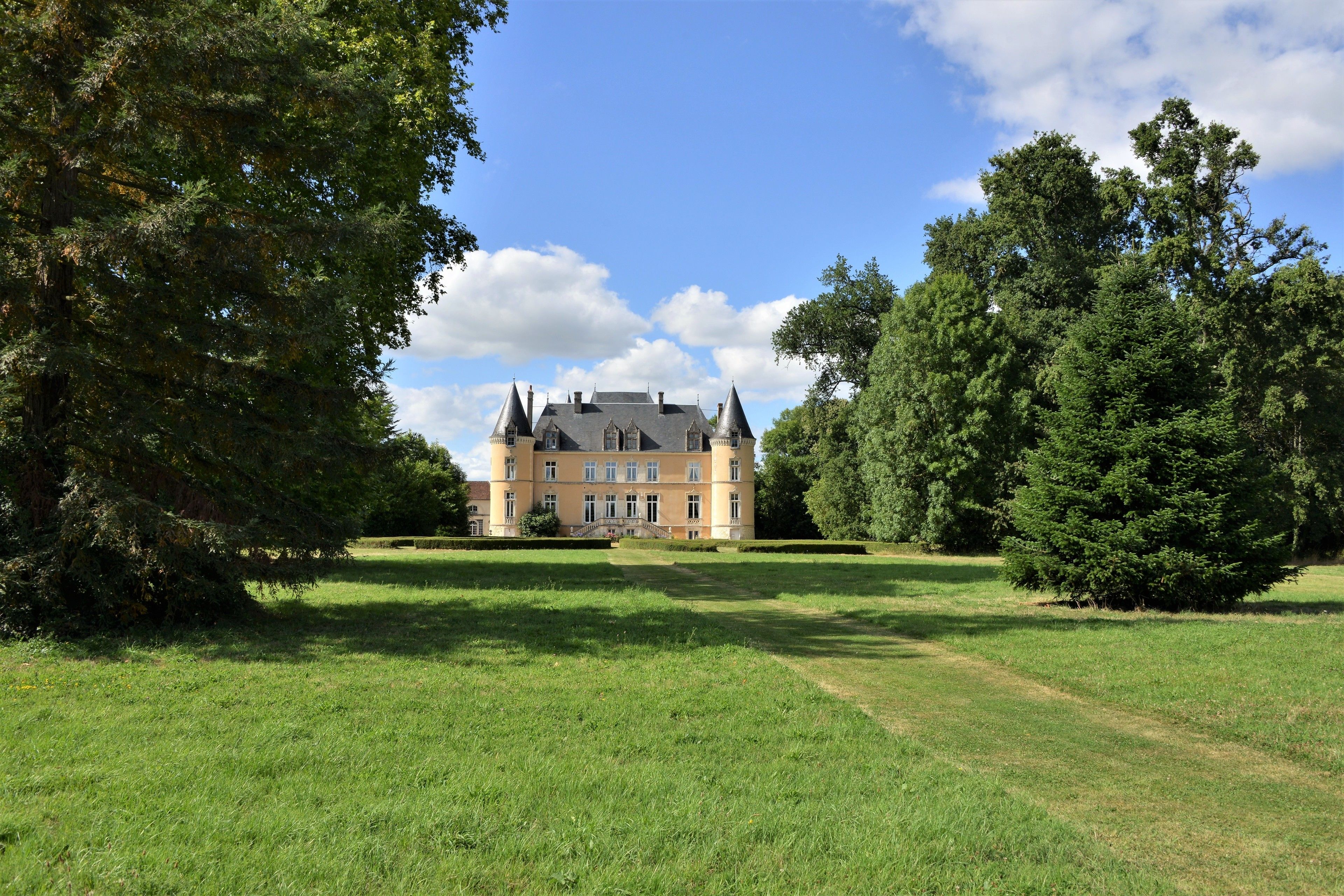 A large, historic building with multiple towers and a well-maintained lawn in front.