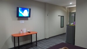 A hotel room with a television mounted on the wall, a small table with a remote control, and a mirror on the opposite wall.