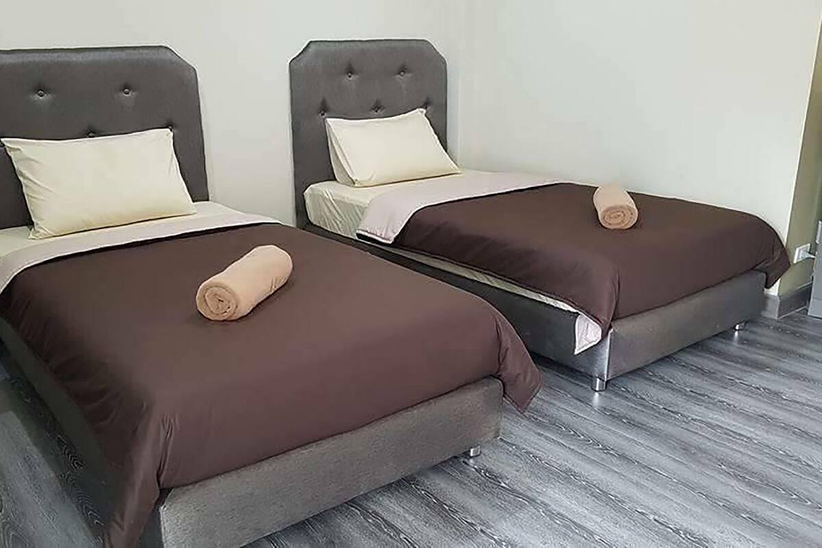 Twee eenpersoonsbedden met donkere hoofdborden en lichtgekleurde beddengoed, een opgerolde handdoek op elk bed, en een houten vloer.