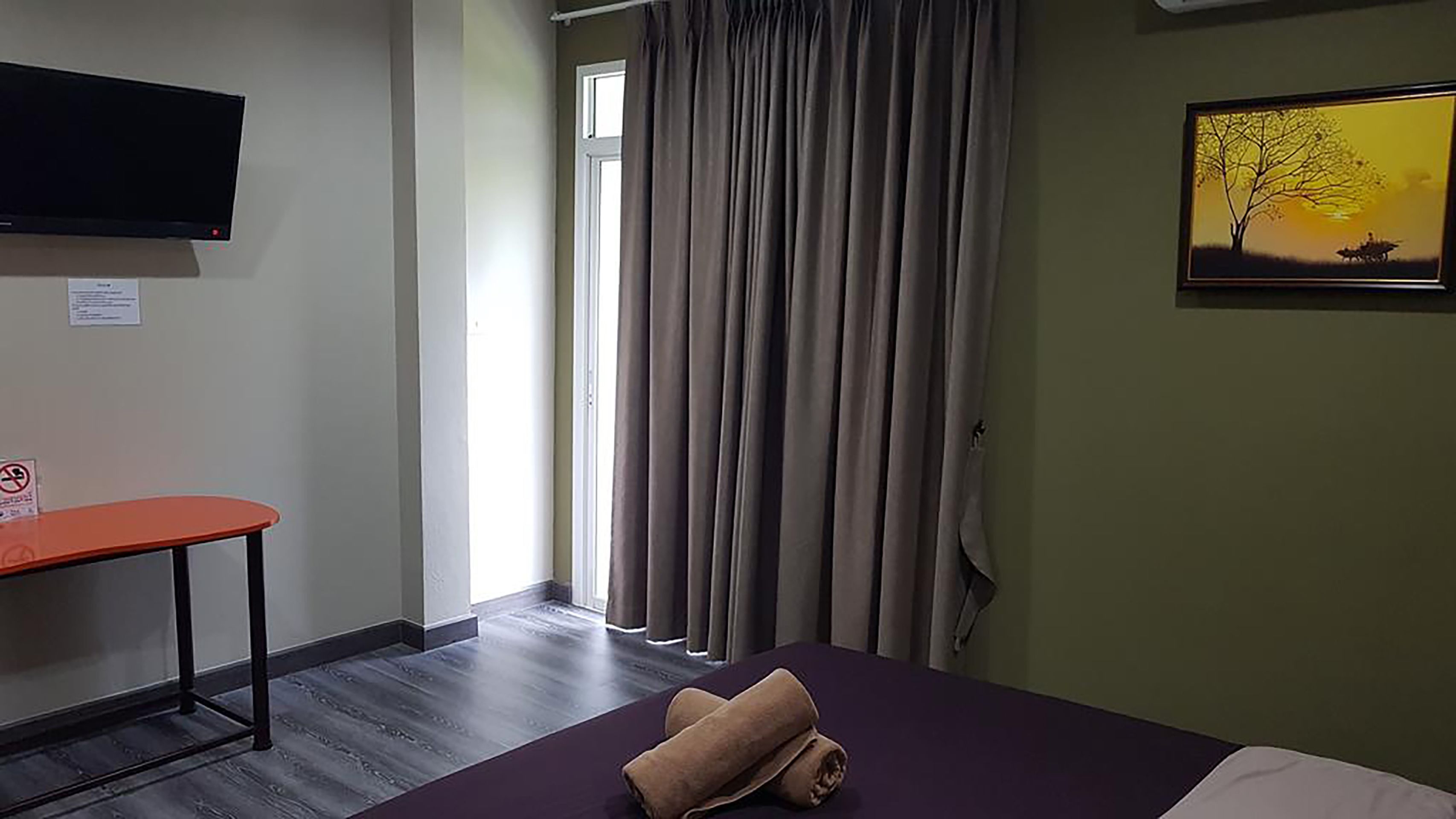 A hotel room with a bed, a desk, a television, a painting, and a window with curtains.