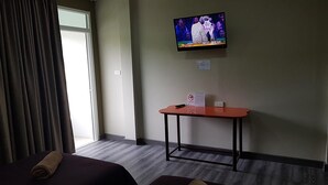 A hotel room with a bed, a small table, a television mounted on the wall, and a window with curtains.