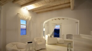 Un dormitorio moderno con decoración blanca, un ventanal grande con vistas al mar, un rincón de descanso acogedor y un banco empotrado.
