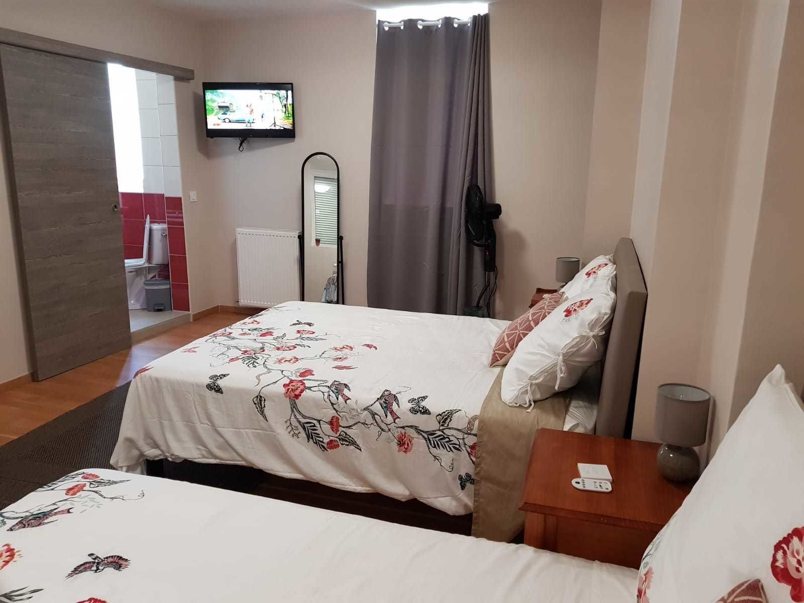 Une chambre d’hôtel avec un lit, un téléviseur fixé au mur, une fenêtre avec des rideaux et une porte donnant sur une salle de bain.