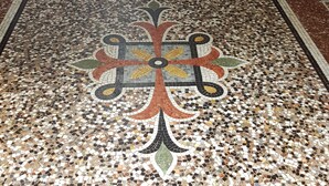 Uma escadaria com tapete vermelho, piso estampado e uma porta.