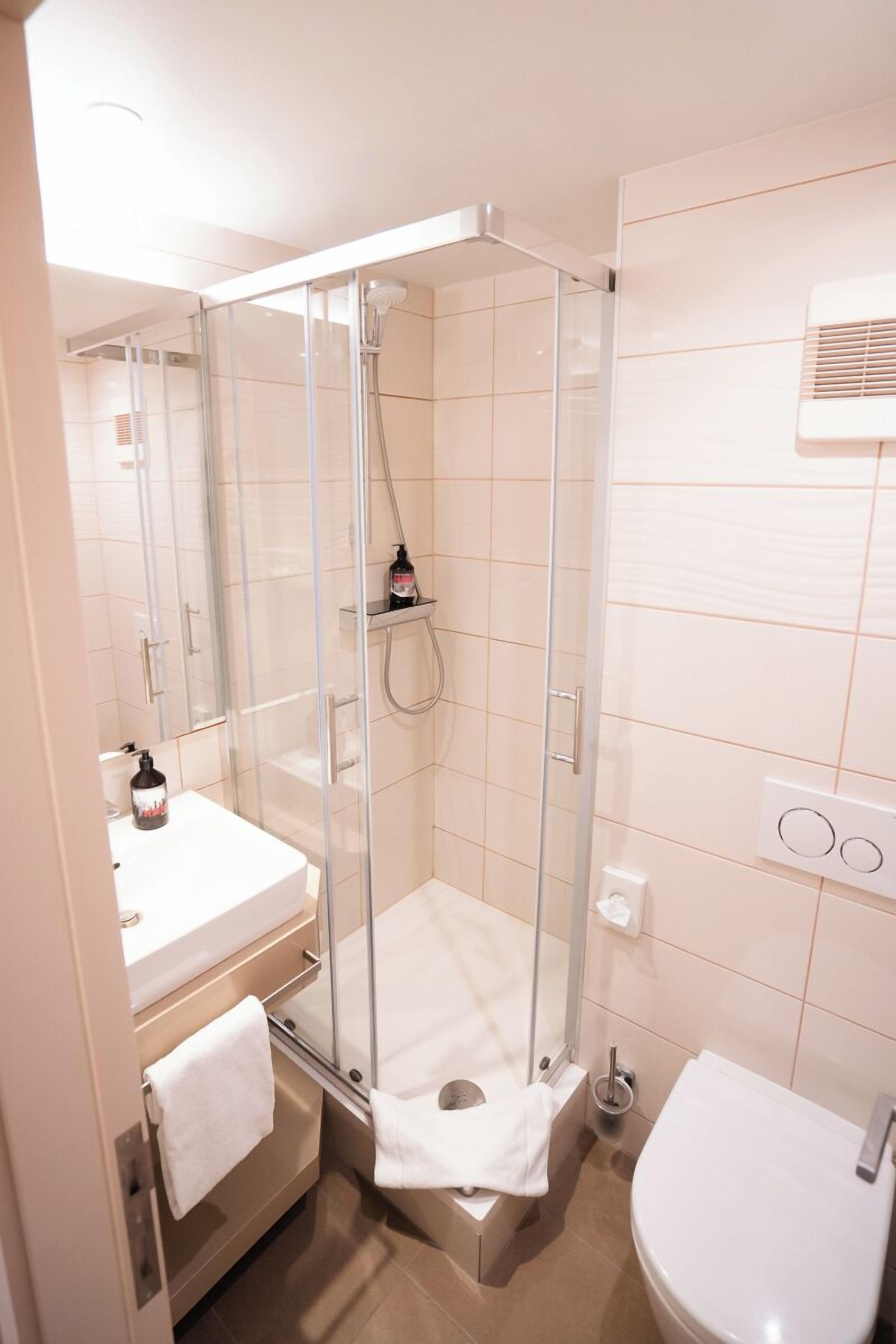 A modern bathroom with a glass-enclosed shower, a white sink, and a toilet.