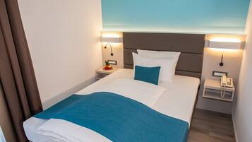 Quarto de hotel com cama, mesas de cabeceira, telefone e luminária fixada na parede.