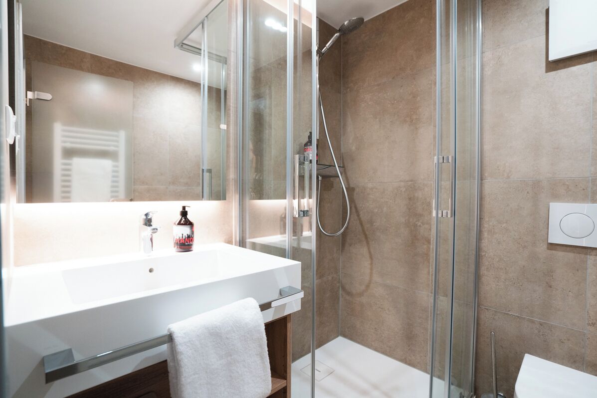 Un baño moderno con ducha envuelta en vidrio, un lavamanos blanco y un espejo.