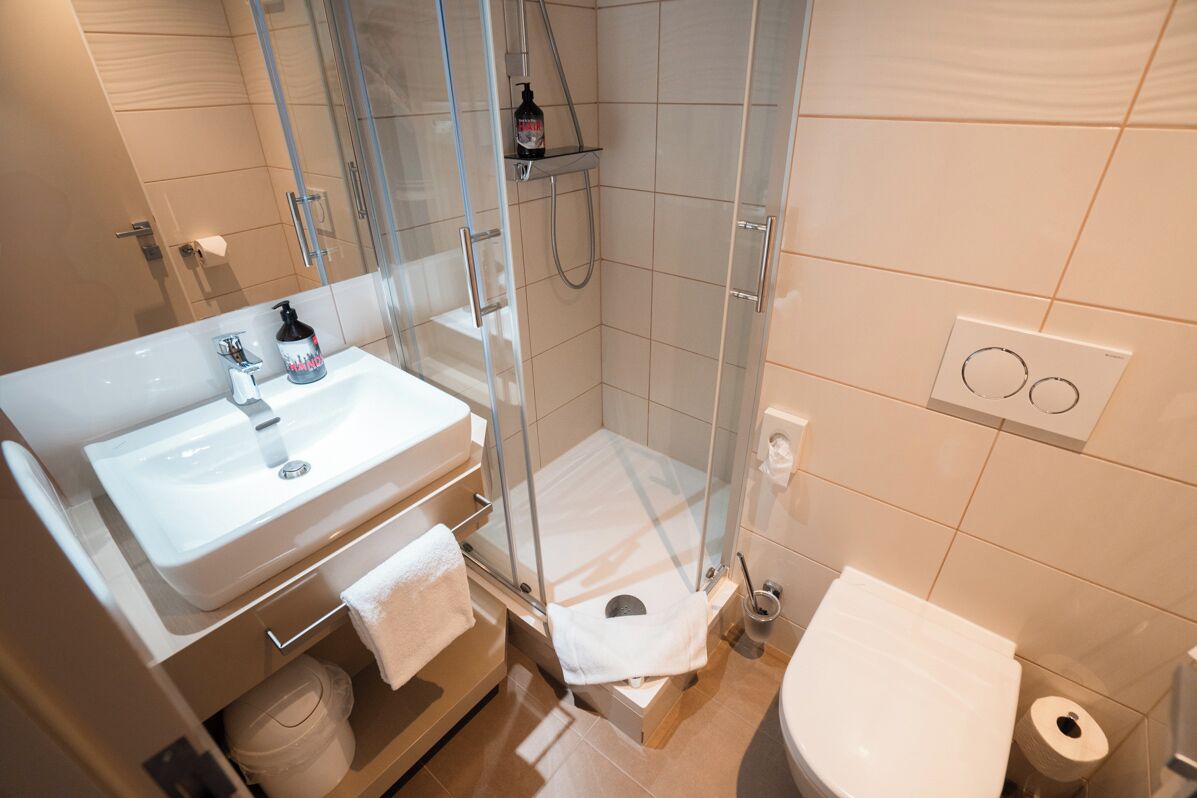 Un baño moderno con ducha envuelta en vidrio, un lavamanos blanco y un inodoro.