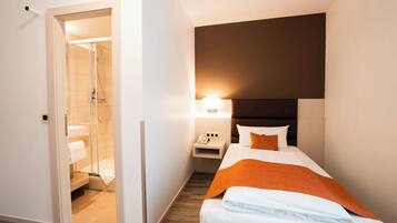 Une chambre d’hôtel comprenant un lit, une table de chevet, une lampe et un espace douche.