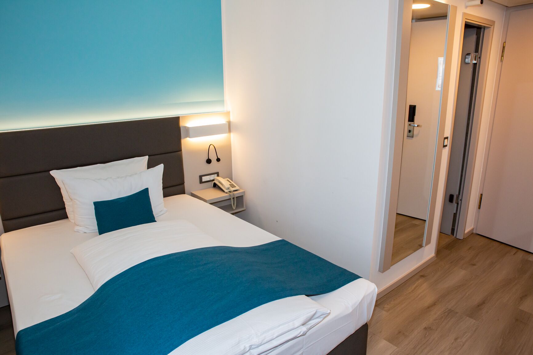 Une chambre d’hôtel moderne avec un grand lit, un téléphone sur la table de chevet et un miroir au mur.