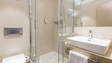 Un baño moderno con ducha de vidrio, lavamanos blanco y retrete.