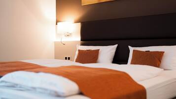Una cama bien tendida con ropa de cama blanca y marrón, un cabecero oscuro y una lámpara de pared.