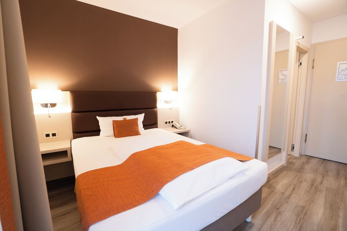 A hotel room with a bed, nightstands, a lamp, and a door.