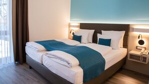Ein modernes Hotelzimmer mit einem großen Bett, zwei Nachttischen, einem Beistelltisch und einem Fenster mit Vorhängen.