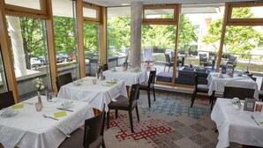 Ein Restaurant mit gedeckten Tischen, großen Fenstern und Blick ins Freie.