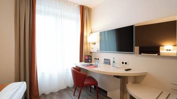 A hotel room with a desk, a chair, a bed, a TV, and a window with curtains.