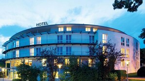 Ein modernes Hotel mit geschwungener Fassade, mehreren Balkonen und einem gut beleuchteten Eingang.