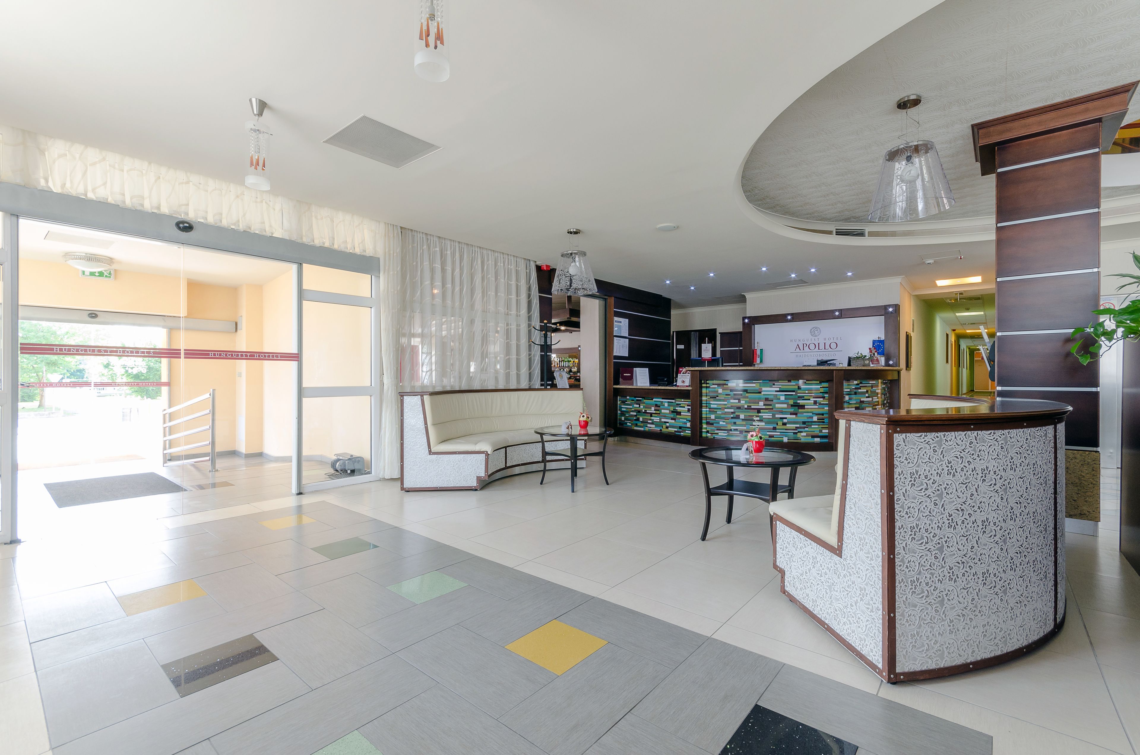 Un vestíbulo de hotel con mostrador de recepción, zona de estar y una escalera que conduce al piso superior.