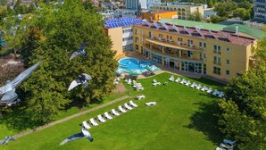 A hotel with a swimming pool surrounded by sun loungers, a rooftop with solar panels, and a lush green lawn. - Hunguest Hotel Apollo (Hajduszoboszlo)