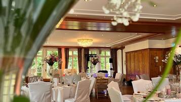 Een feestzaal met ronde tafels, witte tafellakens en stoelen.