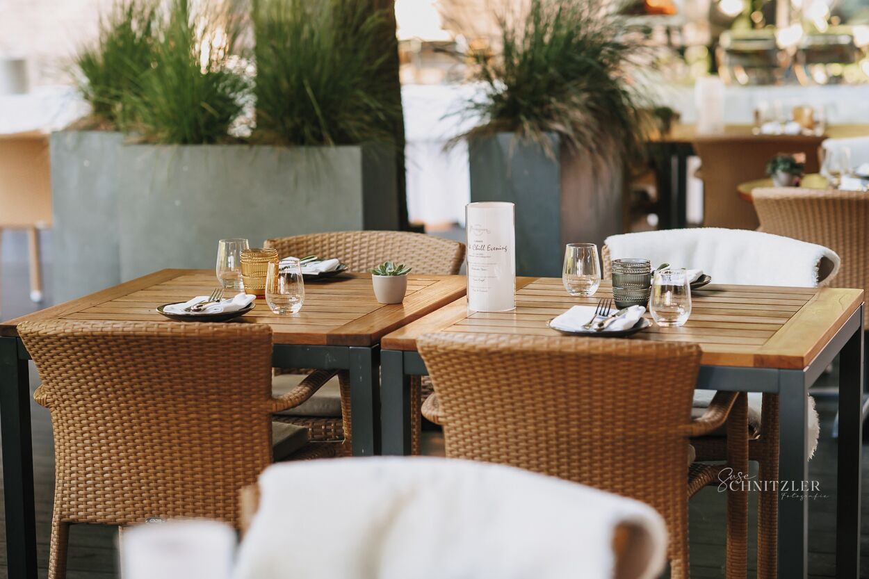 A dining area with wicker chairs and a wooden table set for two, featuring a menu stand and glassware.