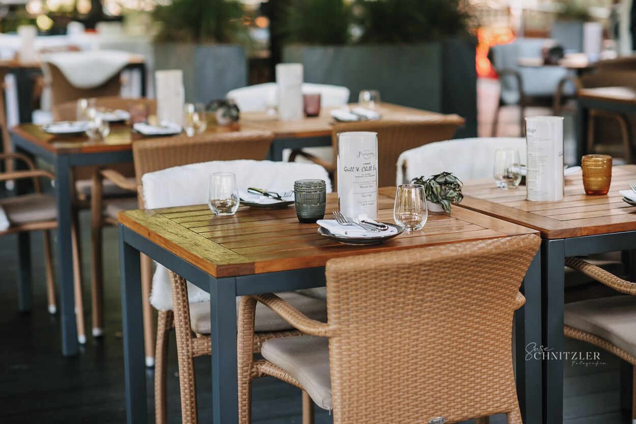 Un ambiente de restaurante con mesas de madera, sillas de mimbre, menús y copas de vino.