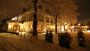 Un hôtel doté d’une cour enneigée, illuminée de lumières chaleureuses, et présentant un style architectural traditionnel avec de nombreuses fenêtres et une entrée imposante.
