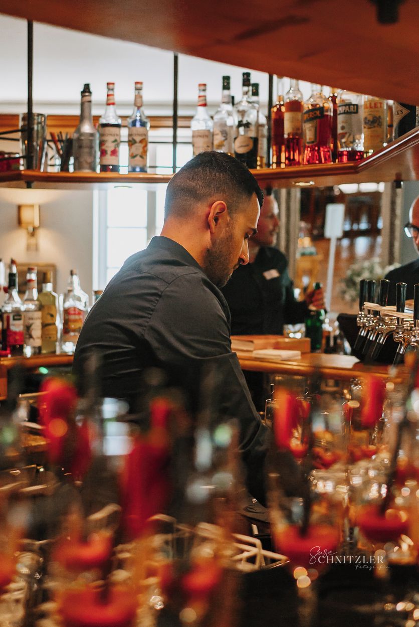 A bar area with shelves of liquor bottles and a bartender preparing drinks.