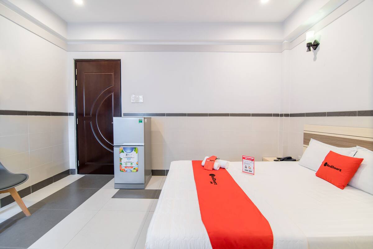A hotel room with a bed, a desk, a refrigerator, and a door.