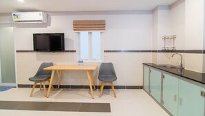 Una cocina compacta con una mesa de madera y dos sillas, un televisor integrado y una ventana con persiana.
