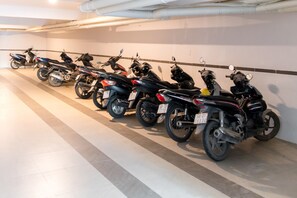 Une rangée de motos est garée dans un parking intérieur bien éclairé, doté d’un sol carrelé et d’un mur blanc orné d’une bordure décorative.