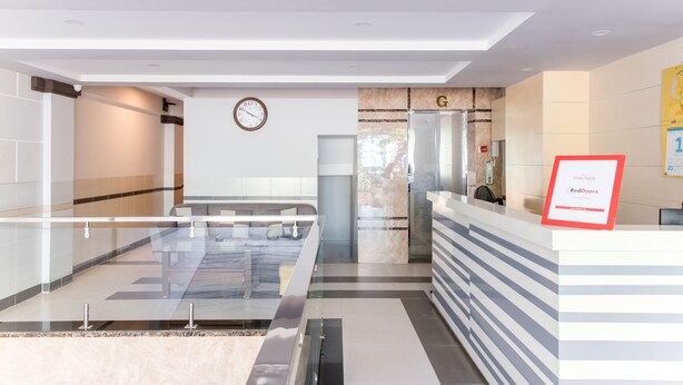 Un área de recepción moderna con un panel de vidrio, un reloj, mostrador de recepción y un letrero que indica una asociación con RedDoorz.