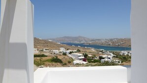 Un pueblo costero con edificios blancos, un cielo azul despejado y vistas al mar y montañas a lo lejos.