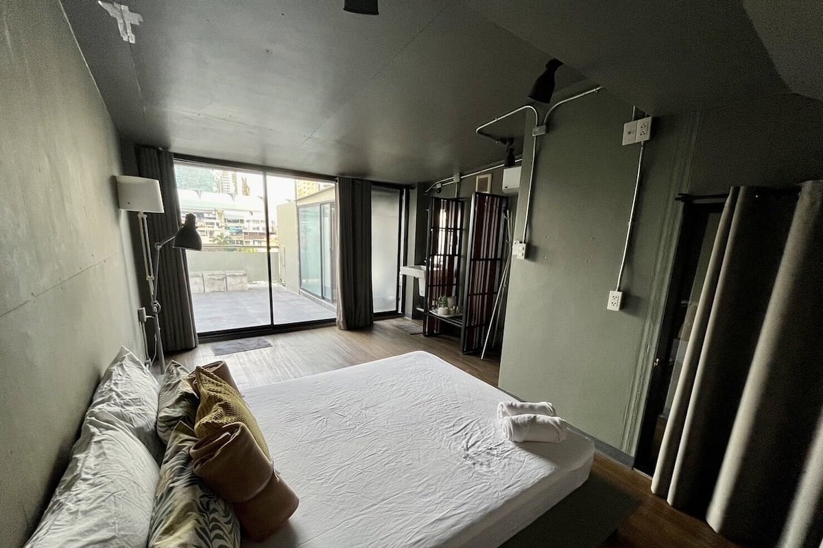 A modern hotel room with a large bed, a desk, and a view of the city through the window.