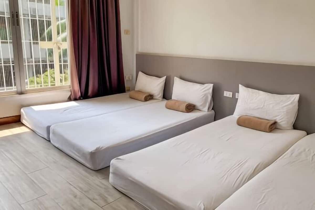 A room with two beds, a window with curtains, and a view of greenery outside.