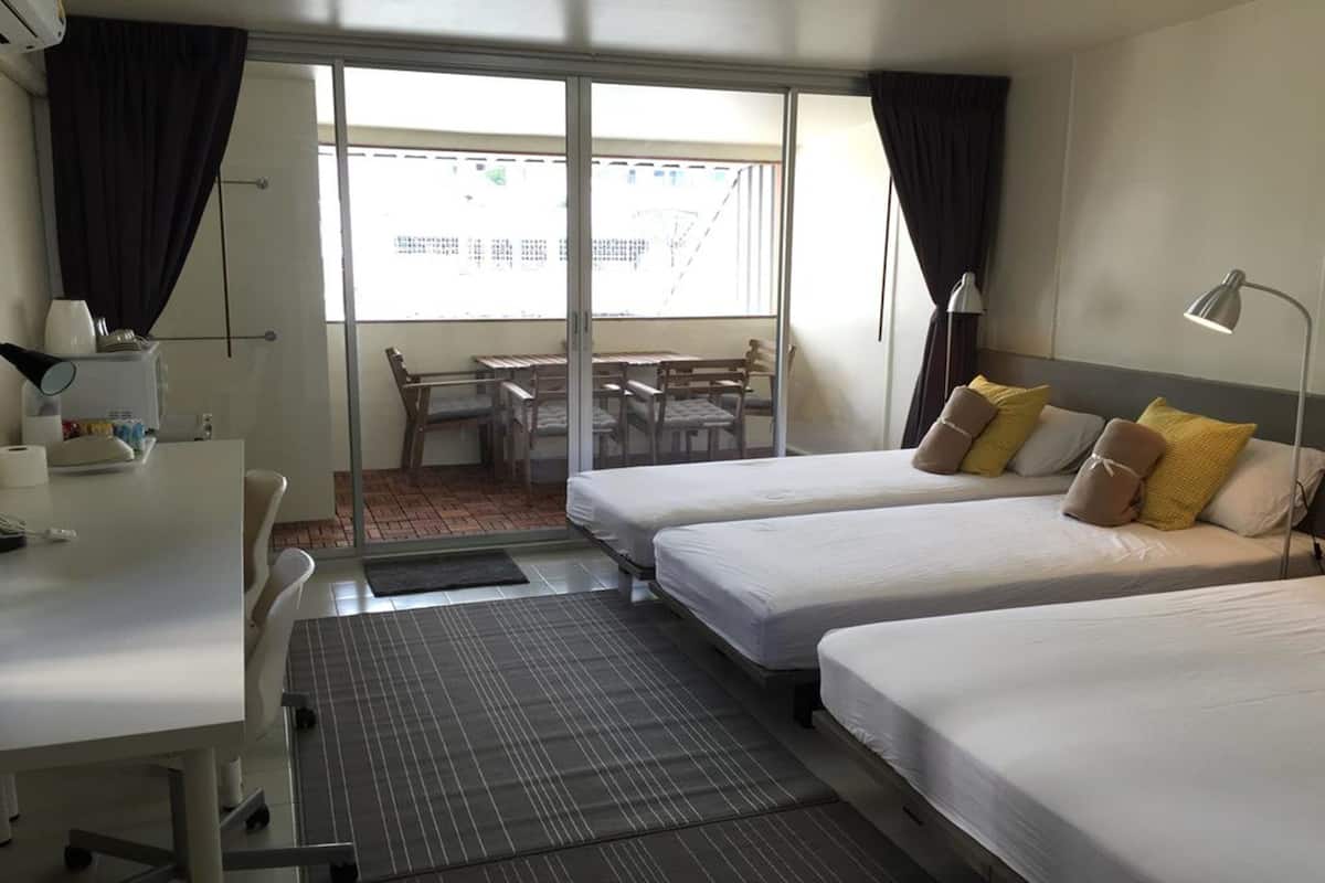 A hotel room with two beds, a desk, a chair, a table, and a view of the outside.